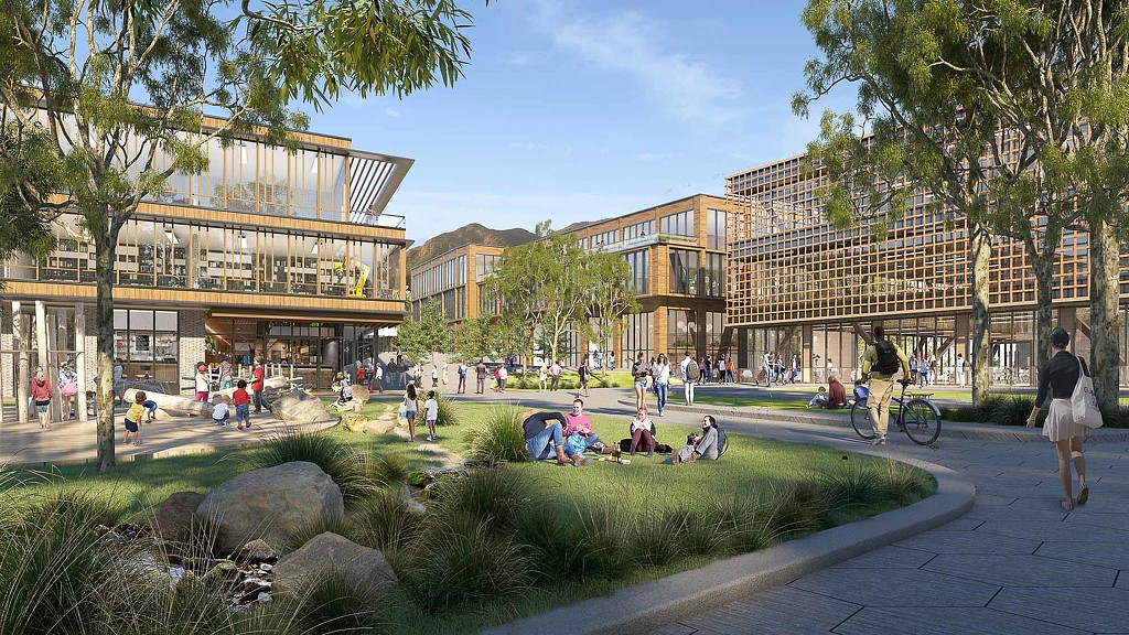 A group of people walking around a park with buildings in the background.